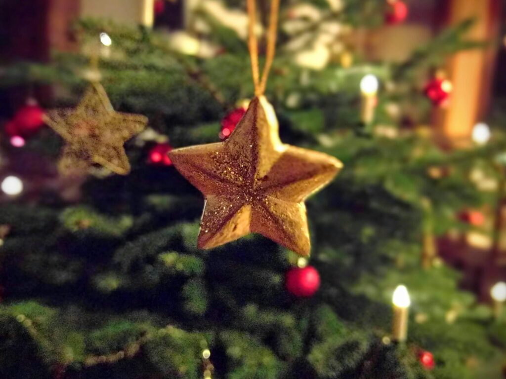 Close-up of a glittery gold star ornament hanging on a Christmas tree, creating a festive atmosphere with sparkling lights.